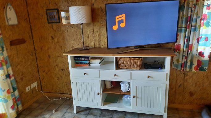 Dressoir met HD LED TV Witte kast met een televisie en lamp, omringd door kleurrijke gordijnen.