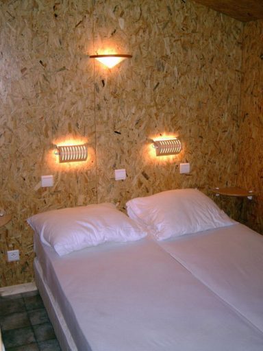 Ouderslaapkamer De ouderslaapkamer met twee eenpersoonsbedden met lichte dekbedden tegen een houten muur. Wandlampen aan beide zijden.