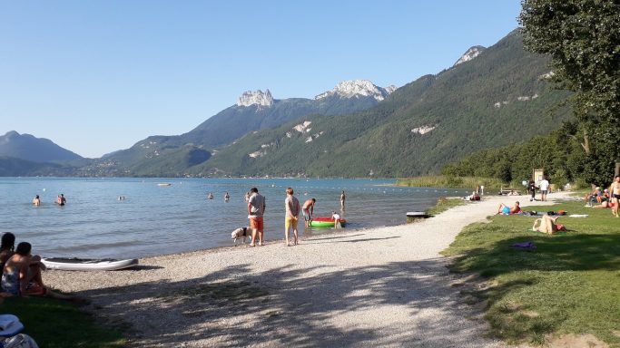 Strand met ligweide Zonnige dag aan een meer met mensen die zwemmen en ontspannen aan de oever.