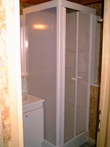 Badkamer met douchecabine Douchecabine met doorschijnende deuren en wastafel ernaast.