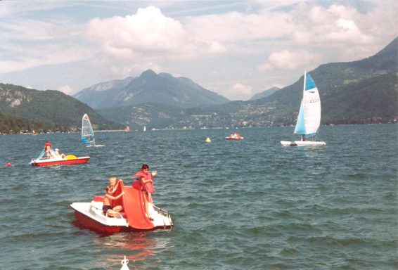 varen èn dobberen Mensen genieten van watersport op meer van Annecy, omgeven door bergen en zeilboten.